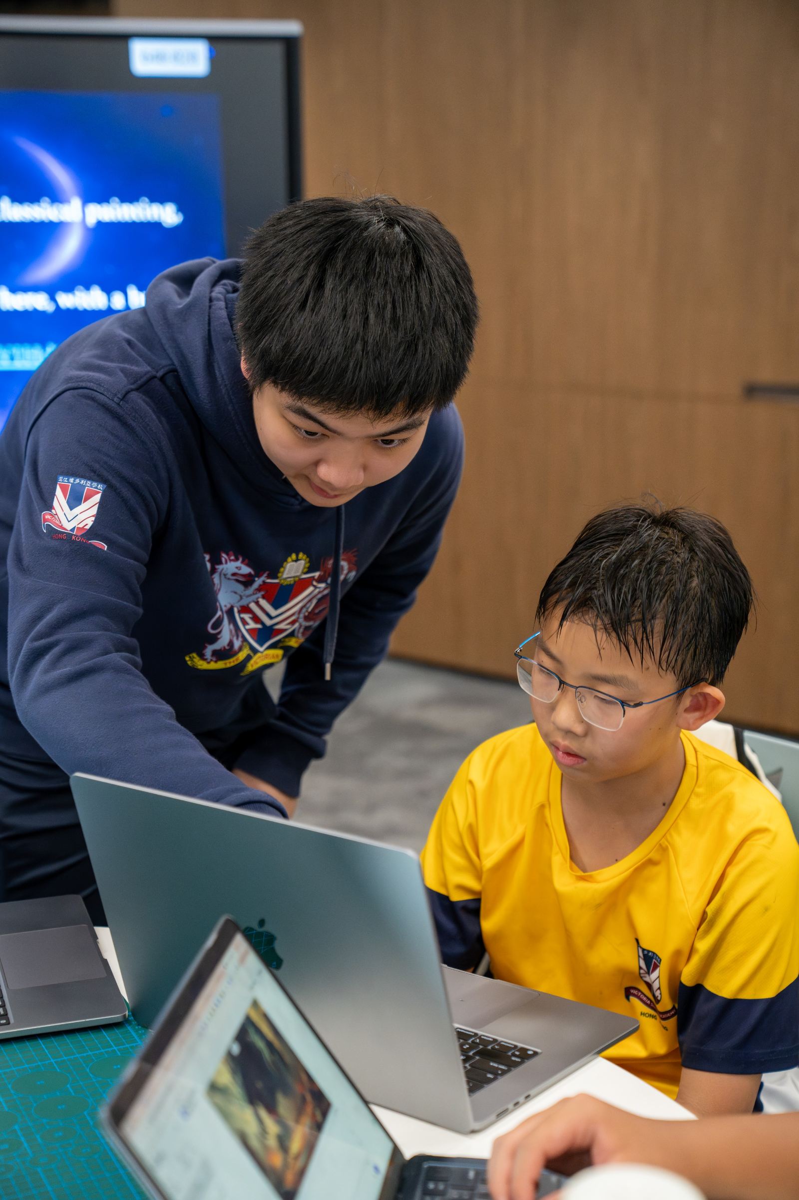 A tutor helps a younger student working at a laptop.