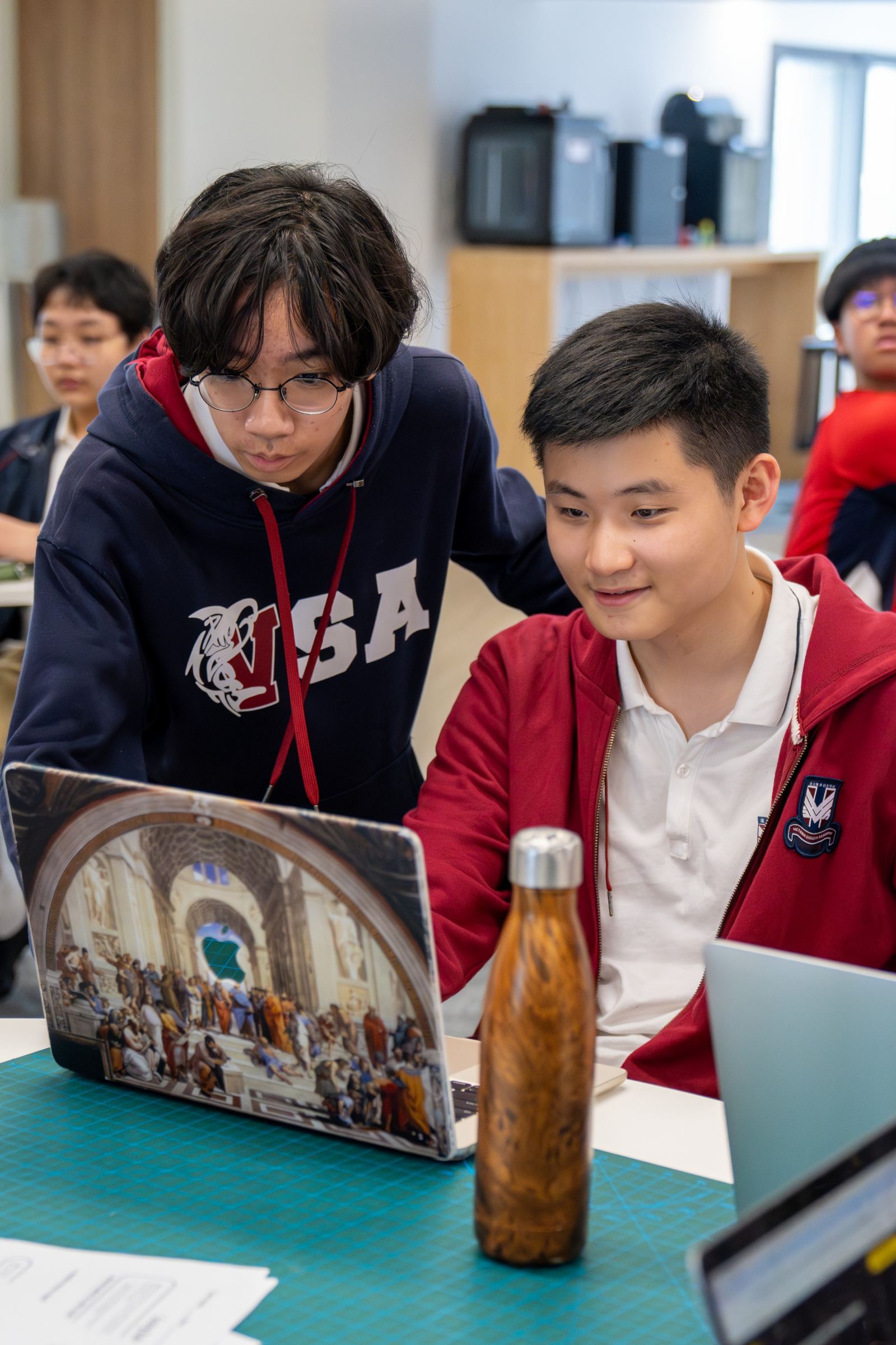 A tutor works through a task beside a student at a laptop.